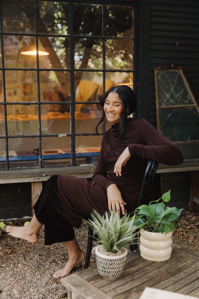 Victoria sitting barefoot on a chair outside an art studio window, laughing with joy.