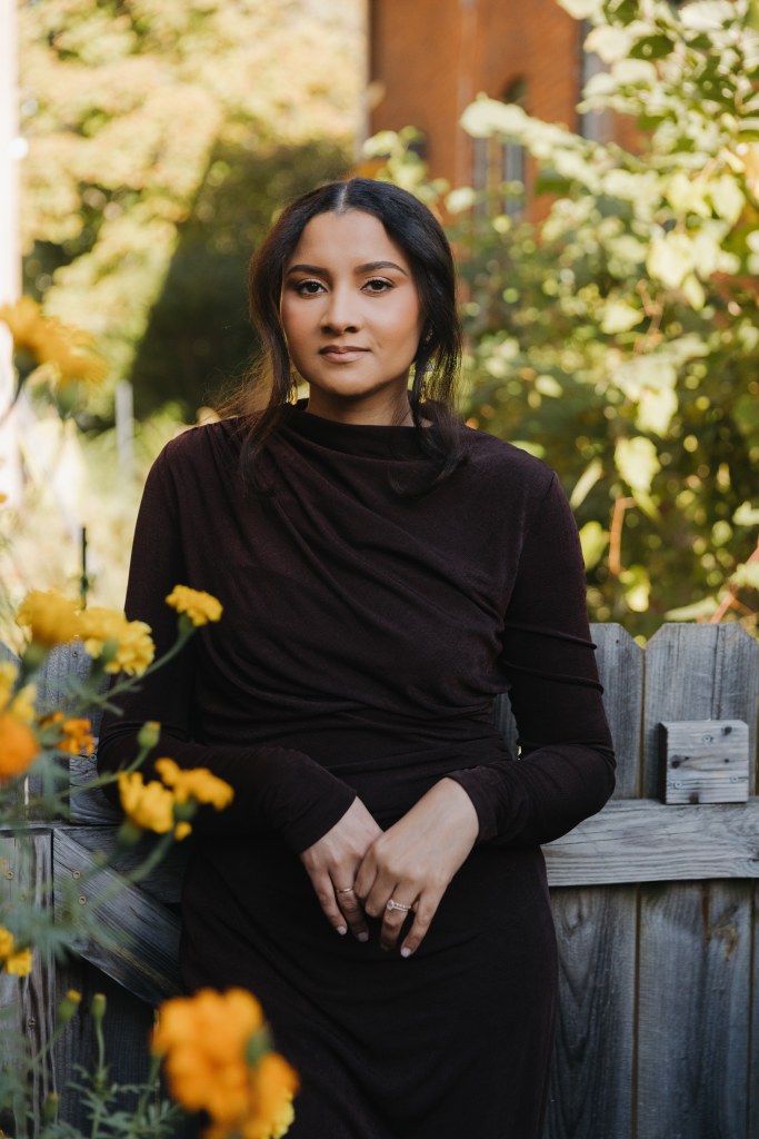 Victoria in a dark dress surrounded by yellow flowers and greenery.